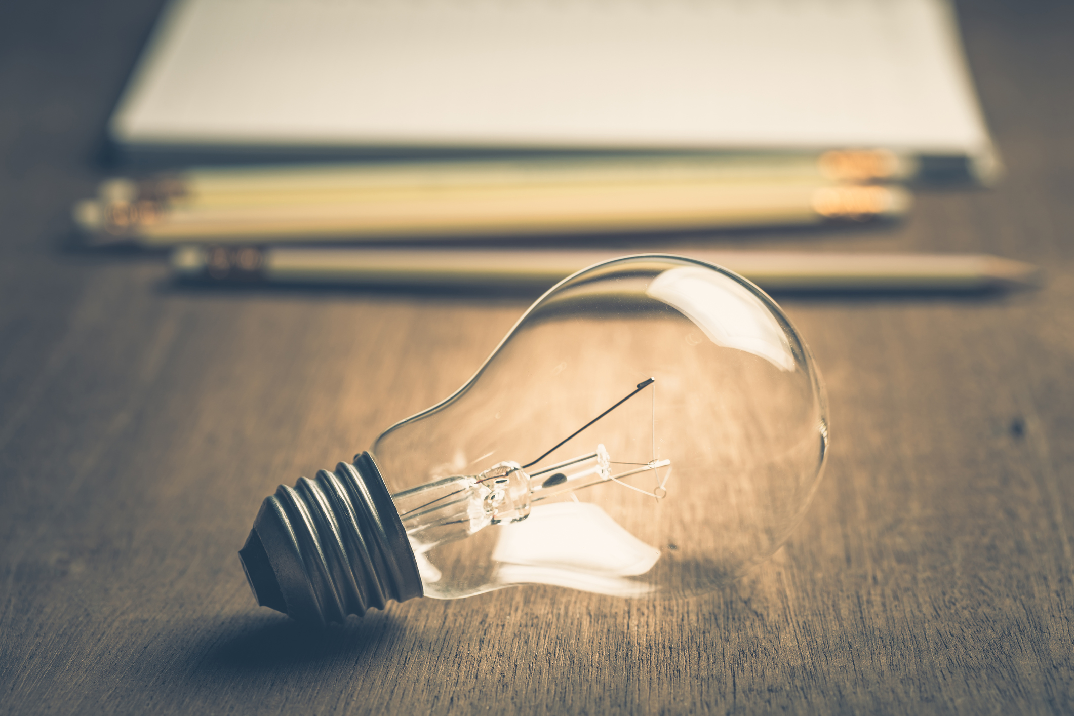 Light bulb with pencils and notebook on background
